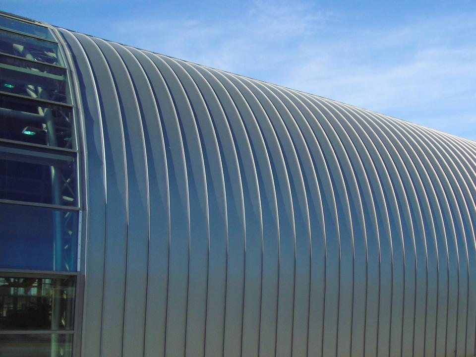 Buet aluminiumstak på en stor hall foran en blå himmel.