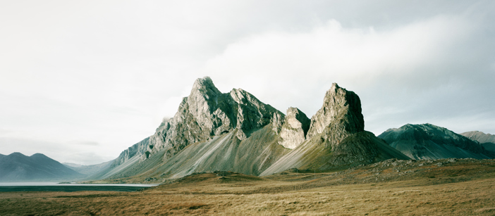 Hills in a grassy setting in front of a cloudy sky.