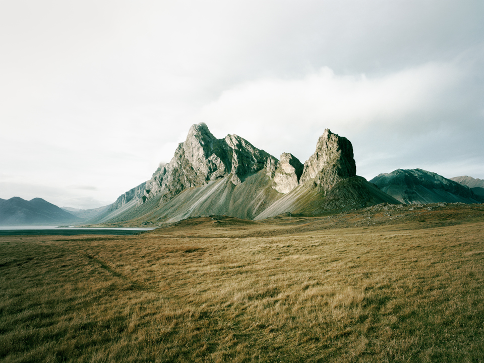 Hills in a grassy setting in front of a cloudy sky.