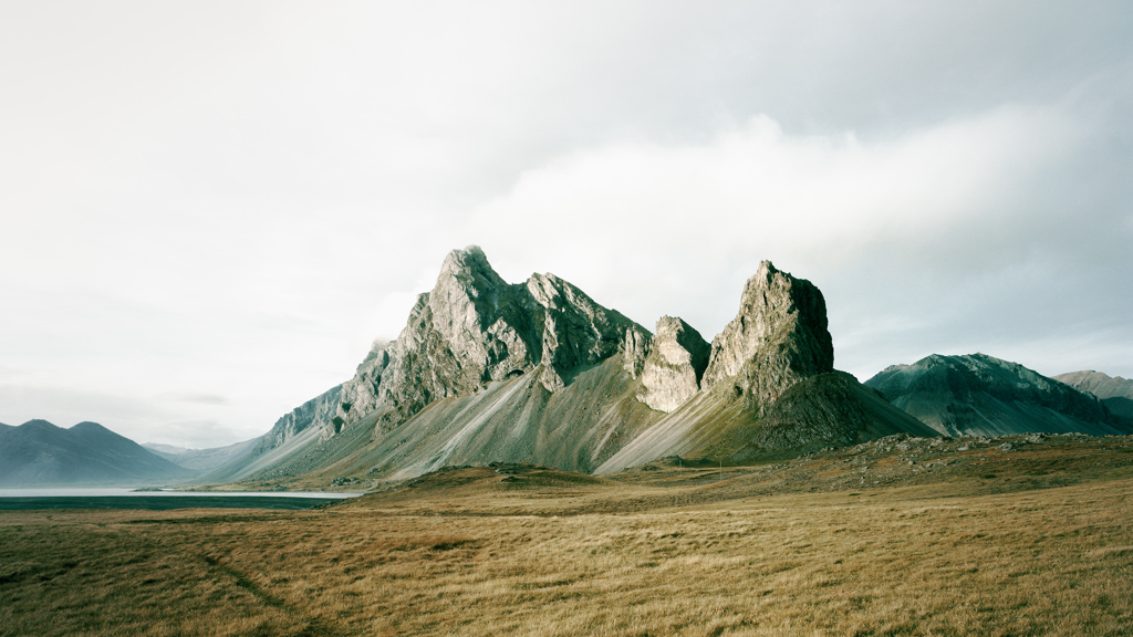 Hills in a grassy setting in front of a cloudy sky.