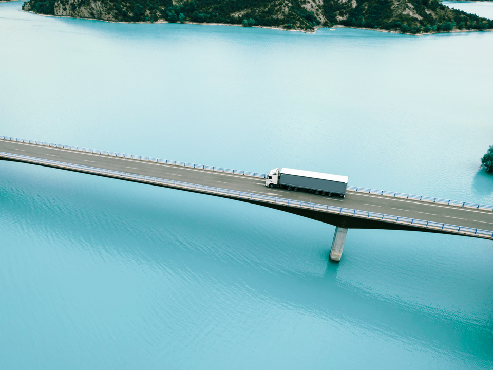 Ein Lastwagen fährt über eine Brücke, die über ein Gewässer führt.