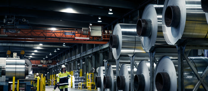 Fabrikkarbeider på Speira-fabrikken står ved siden av oppstablede aluminiumspoler.
