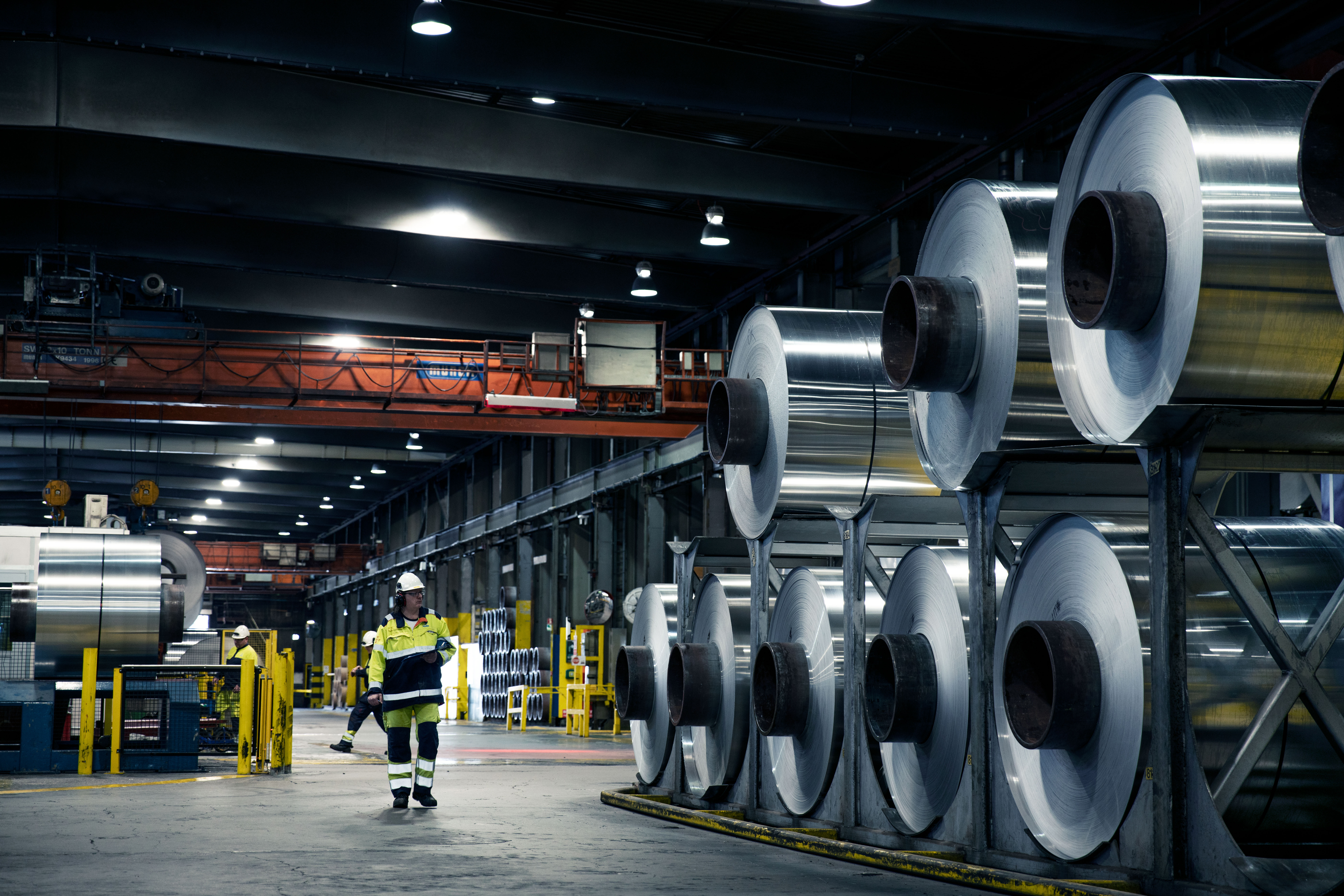 Aluminium coils stacked up in a factory with a Speira employee standing next to them.