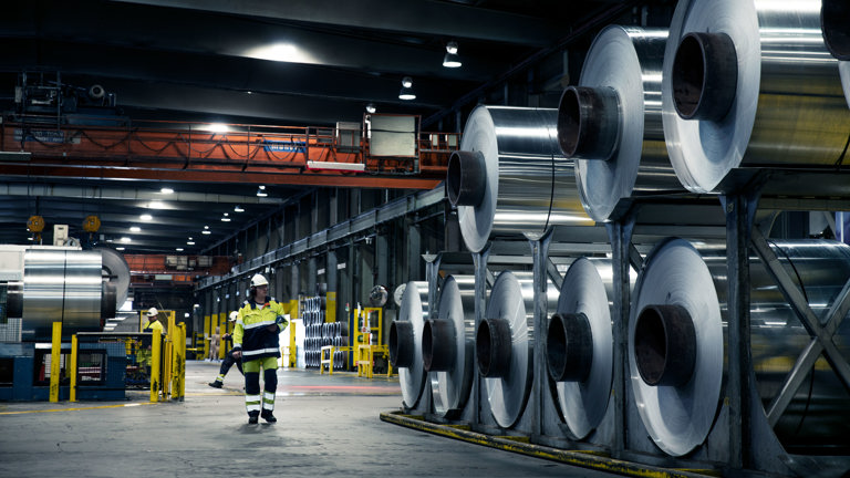 Aluminium coils stacked up in a factory with a Speira employee standing next to them.