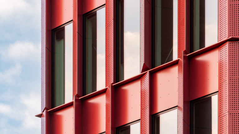 Windows of a building surrounded by a red aluminium façade. 