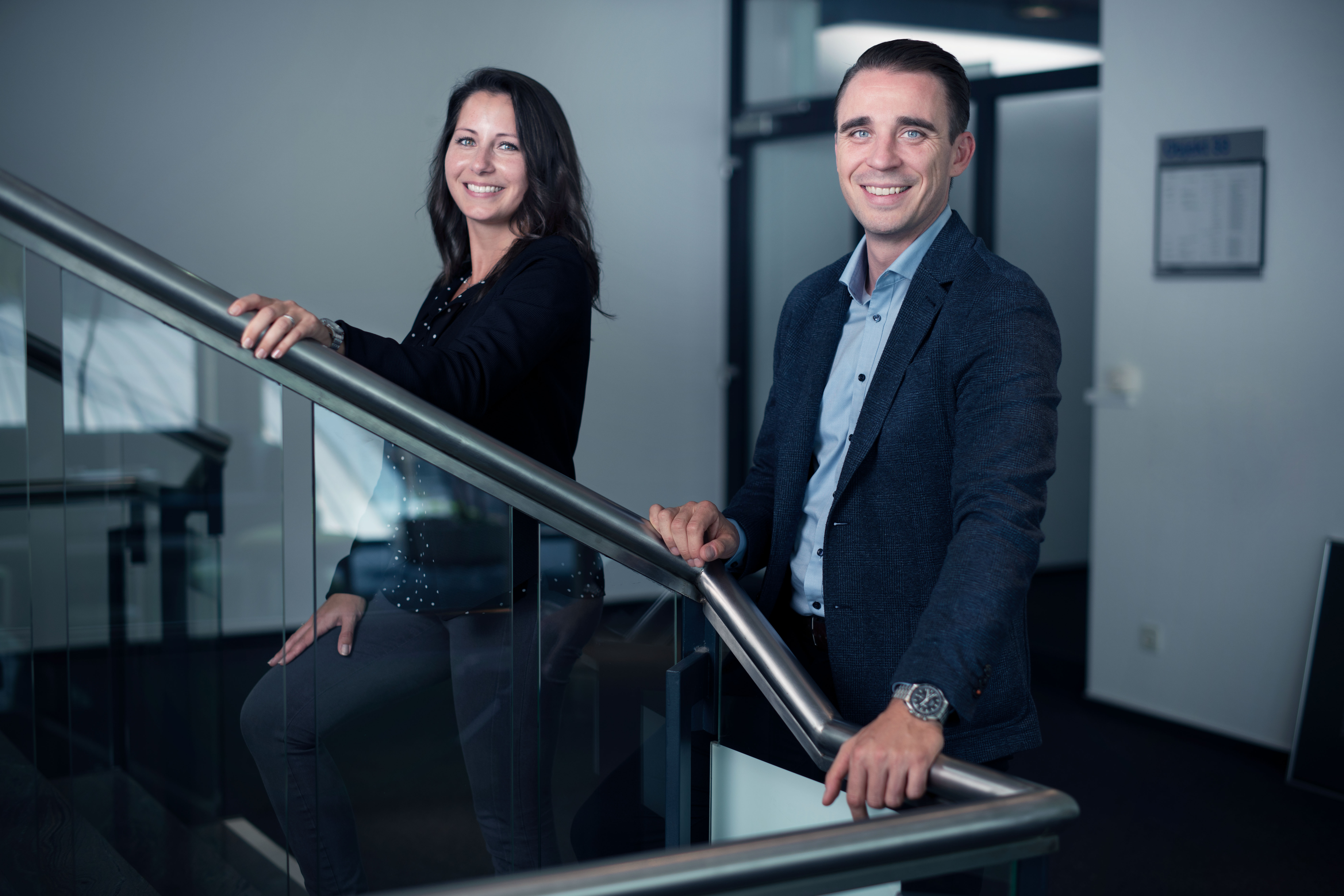 Two smiling employees in office attire on a staircase in the Speira office.