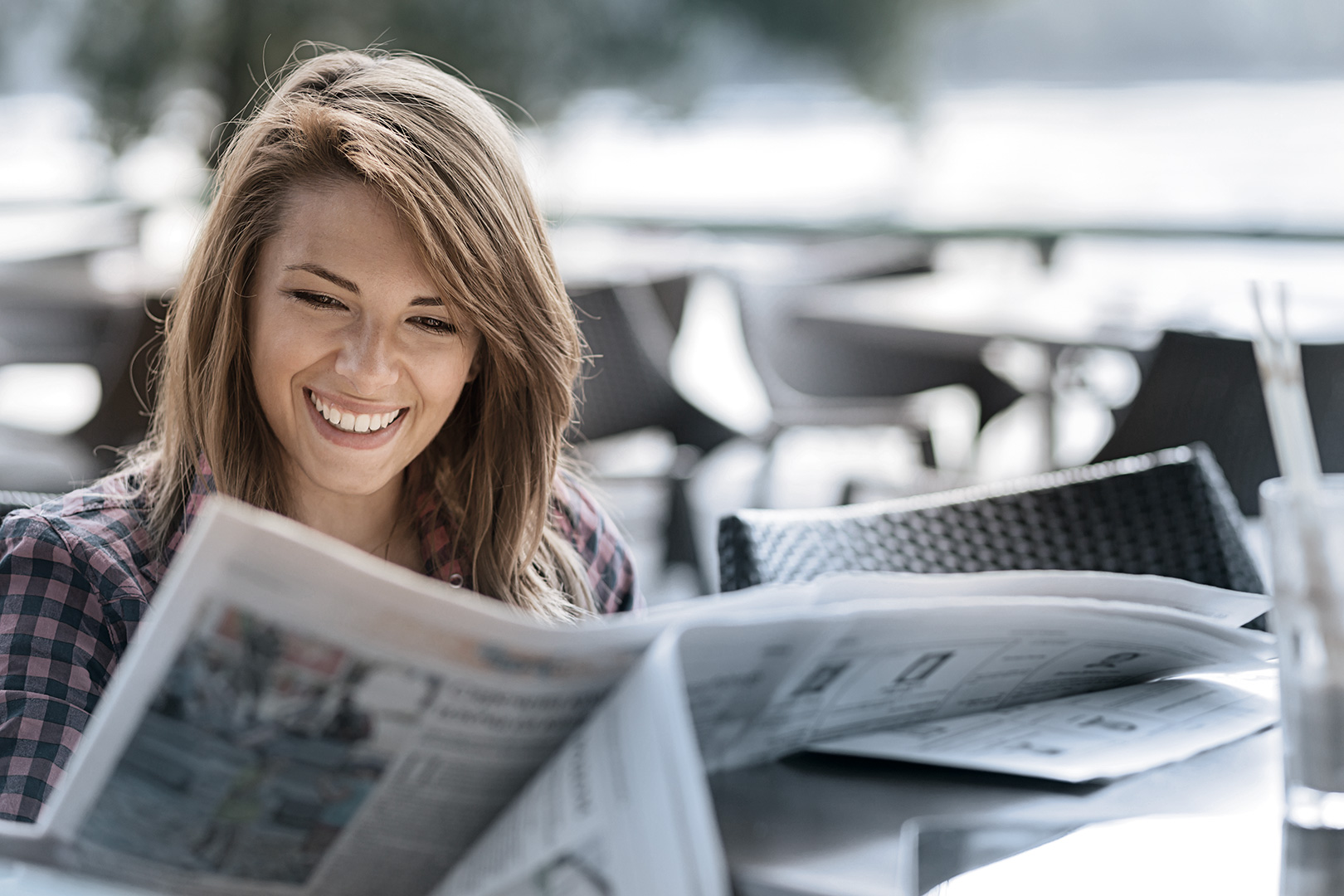 En kvinne sitter utenfor, leser en avis og smiler.