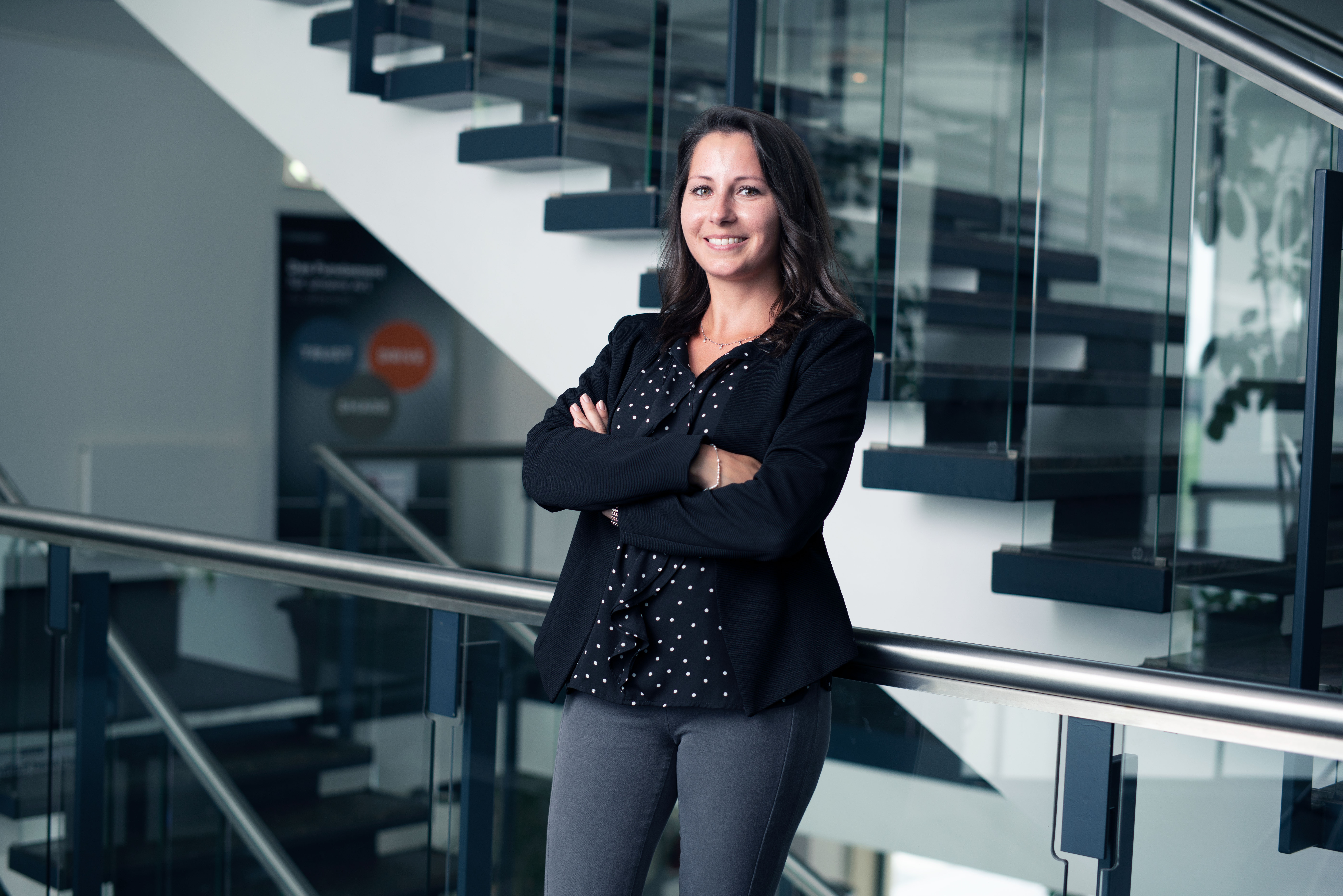 A smiling Speira employee in office attire next to a staircase in an office.