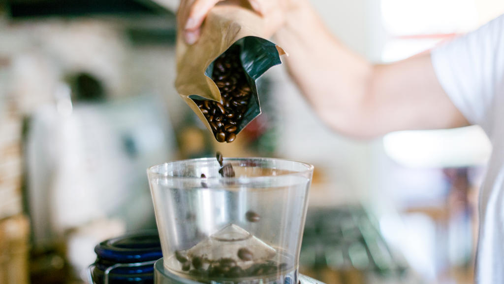 Kaffeebohnen aus einem Aluminiumbeutel, die in eine Kaffeemühle eingefüllt werden.