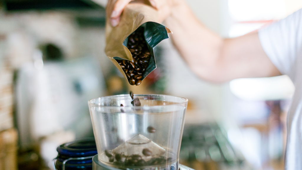 Kaffebønner fra en aluminiumspose helles i en kvernmaskin.