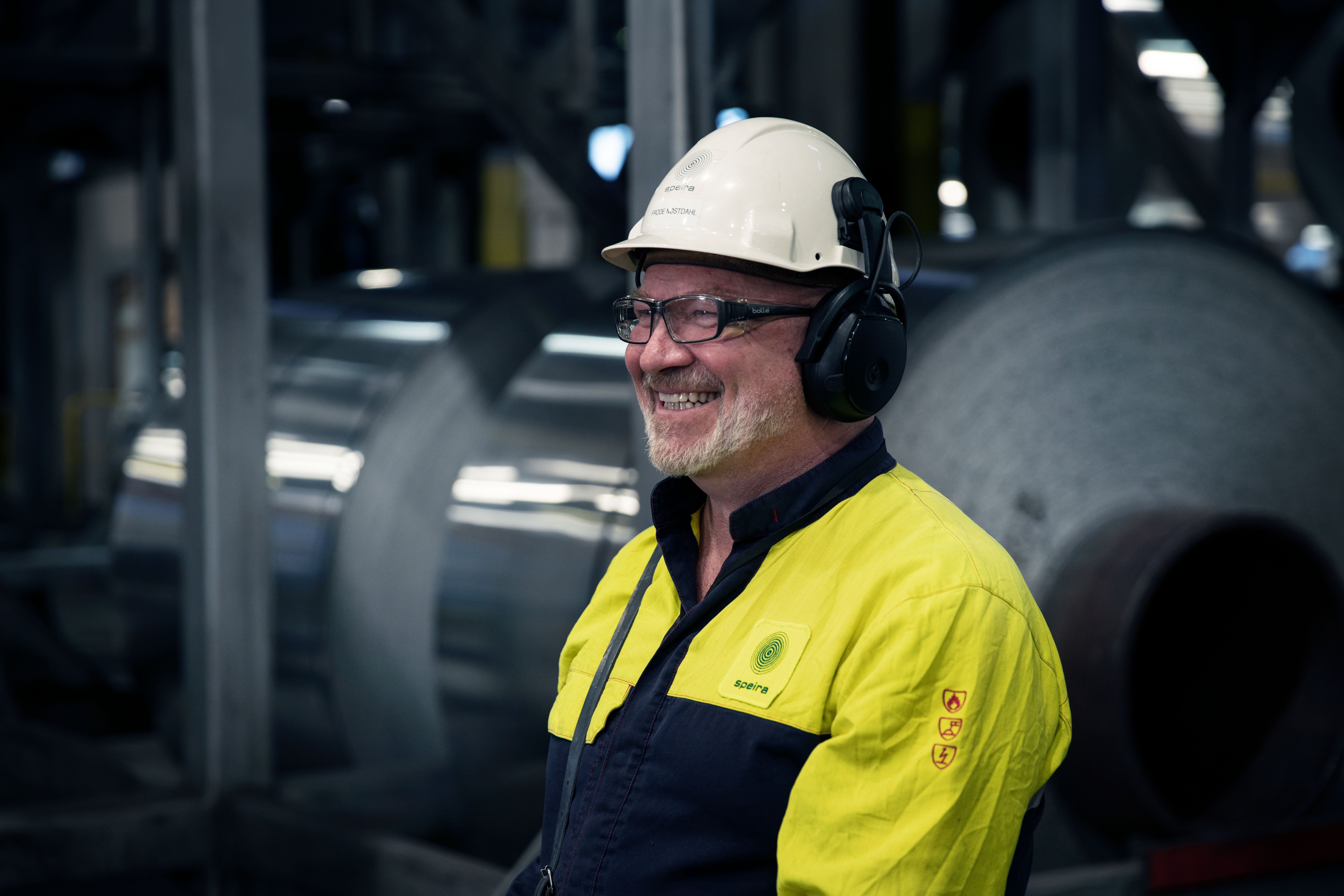 En smilende Speira-ansatt i arbeidsklær foran en aluminiumspole.