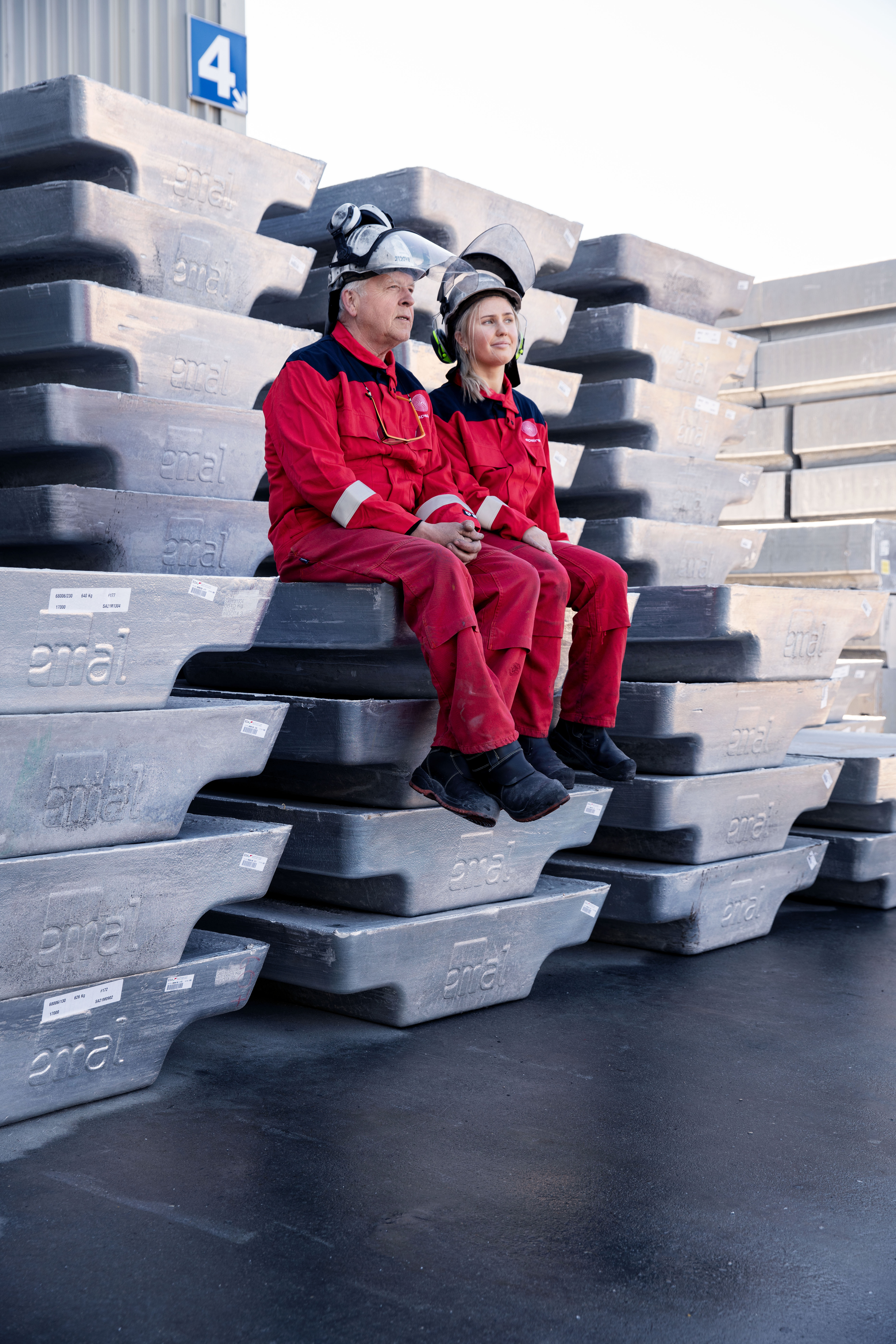 Zwei Speira Mitarbeitende in Arbeitskleidung sitzen auf Aluminiumbarren.