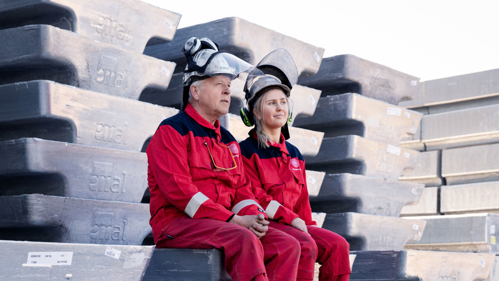 Two Speira employees in work clothes sit on aluminum ingots.