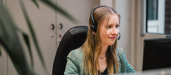 Eine junge Speira Mitarbeiterin sitzt mit Headset an ihrem Schreibtisch im Büro.