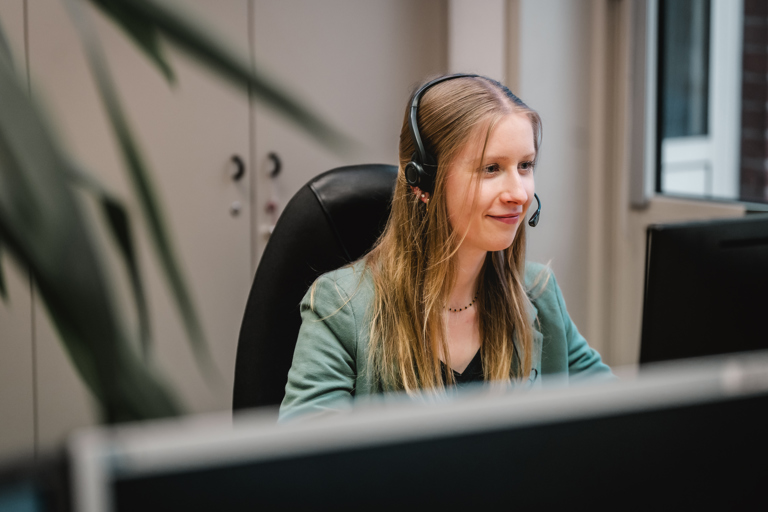 Eine junge Speira Mitarbeiterin sitzt mit Headset an ihrem Schreibtisch im Büro.