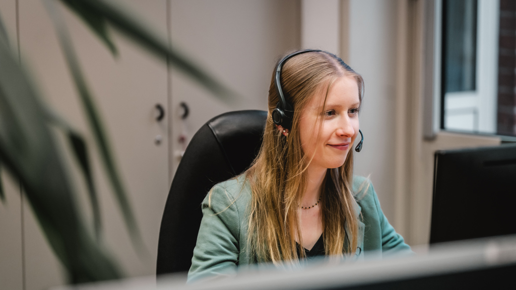 A young Speira employee sits at her desk in the office wearing a headset.