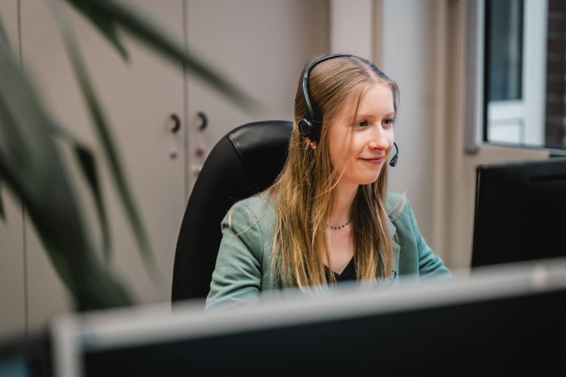 Eine junge Speira Mitarbeiterin sitzt mit Headset an ihrem Schreibtisch im Büro.