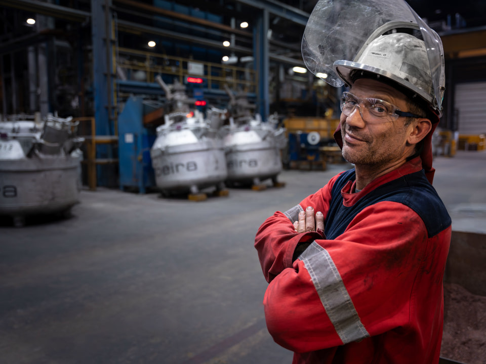 En smilende ansatt står i arbeidsklær på en fabrikk i Speira.