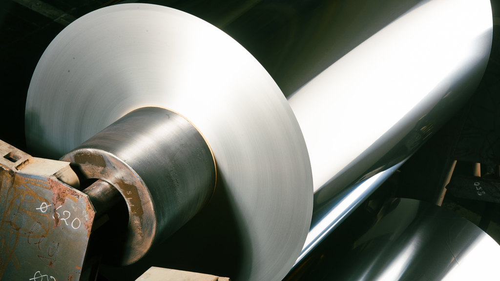 Aluminiumspole som reflekterer et stort, skinnende lys i en fabrikk.