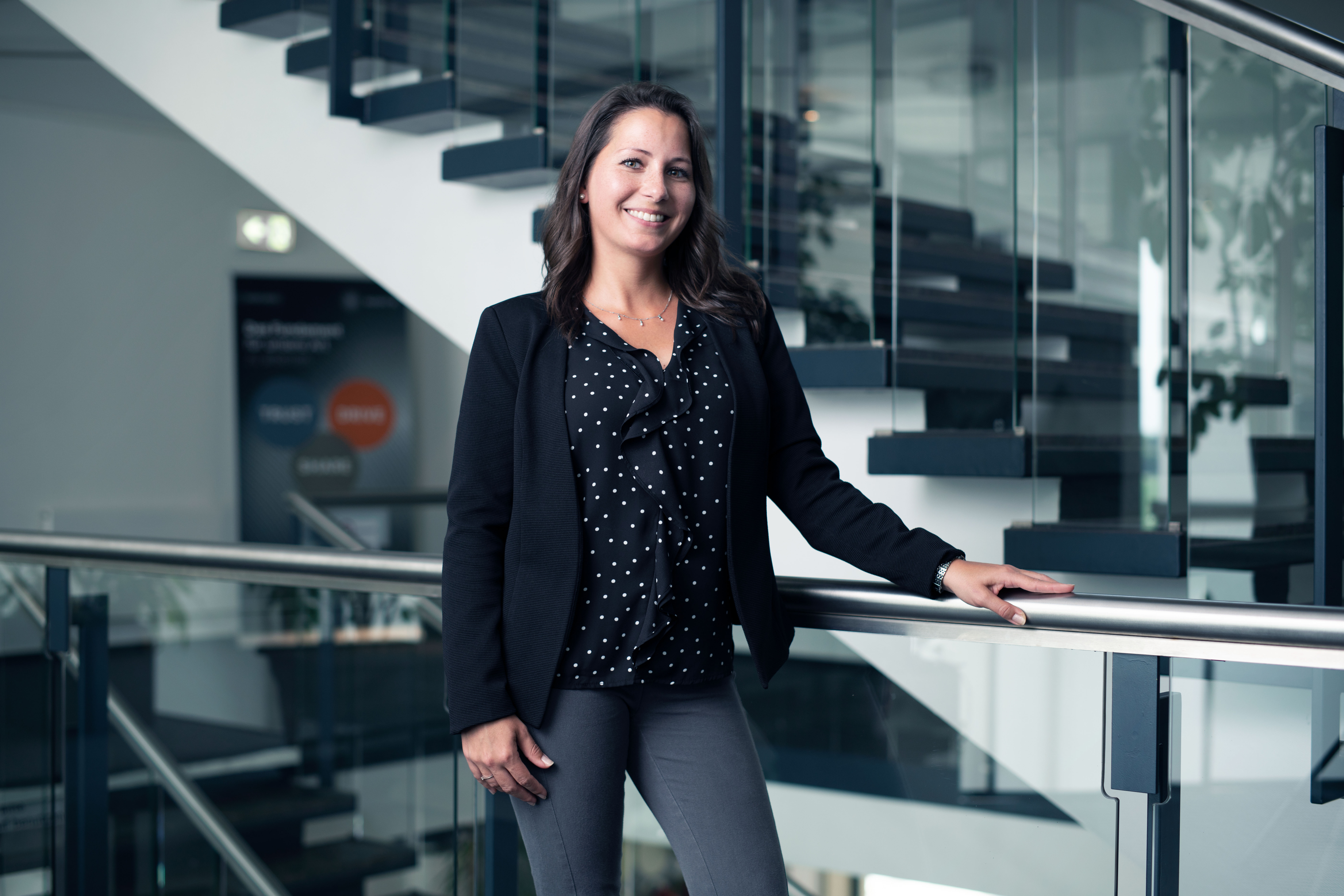 A smiling Speira employee in office attire next to a staircase in an office.