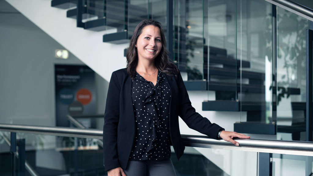 A smiling Speira employee in office attire next to a staircase in an office.