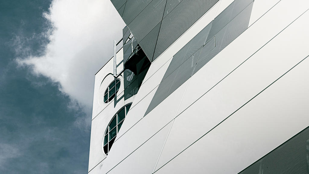Weiße Aluminiumpaneelfassade eines Gebäudes, in der sich das Sonnenlicht spiegelt.