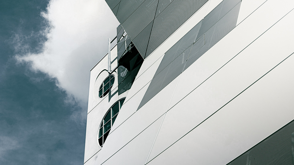 Weiße Aluminiumpaneelfassade eines Gebäudes, in der sich das Sonnenlicht spiegelt.