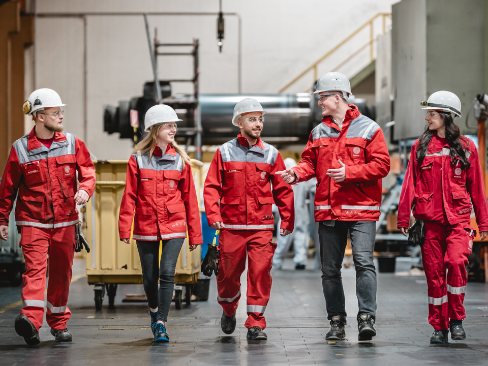 Gruppebilde av fem Speira-ansatte som snakker sammen mens de går gjennom fabrikken.