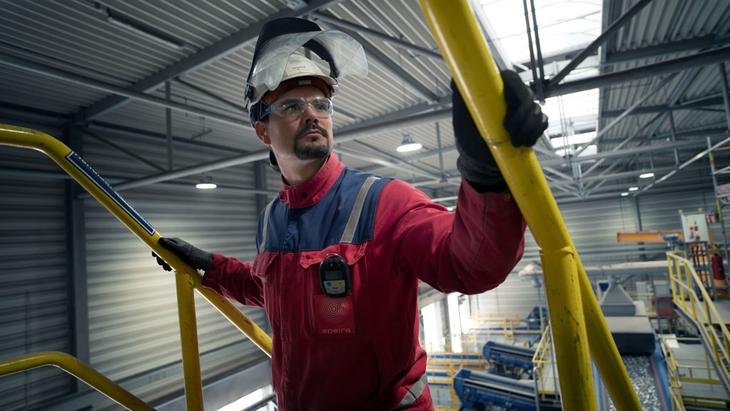 Ein Speira Mitarbeiter in Arbeitskleidung hält sich am gelben Handlauf einer Treppe fest.