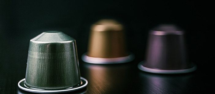 Flerfargede kaffekapsler i aluminium på en svart overflate.