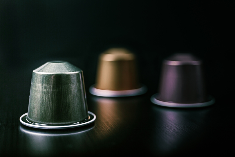 Flerfargede kaffekapsler i aluminium på en svart overflate.